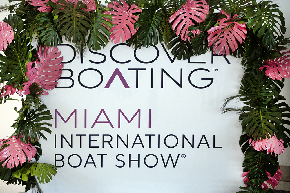 Discover Boating Miami International Boat Show sign framed by tropical green and pink foliage display