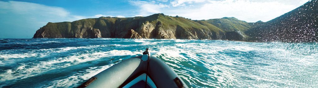 RIB bow approaching rugged cliffs with white water and Atlantic swell under blue skies.
