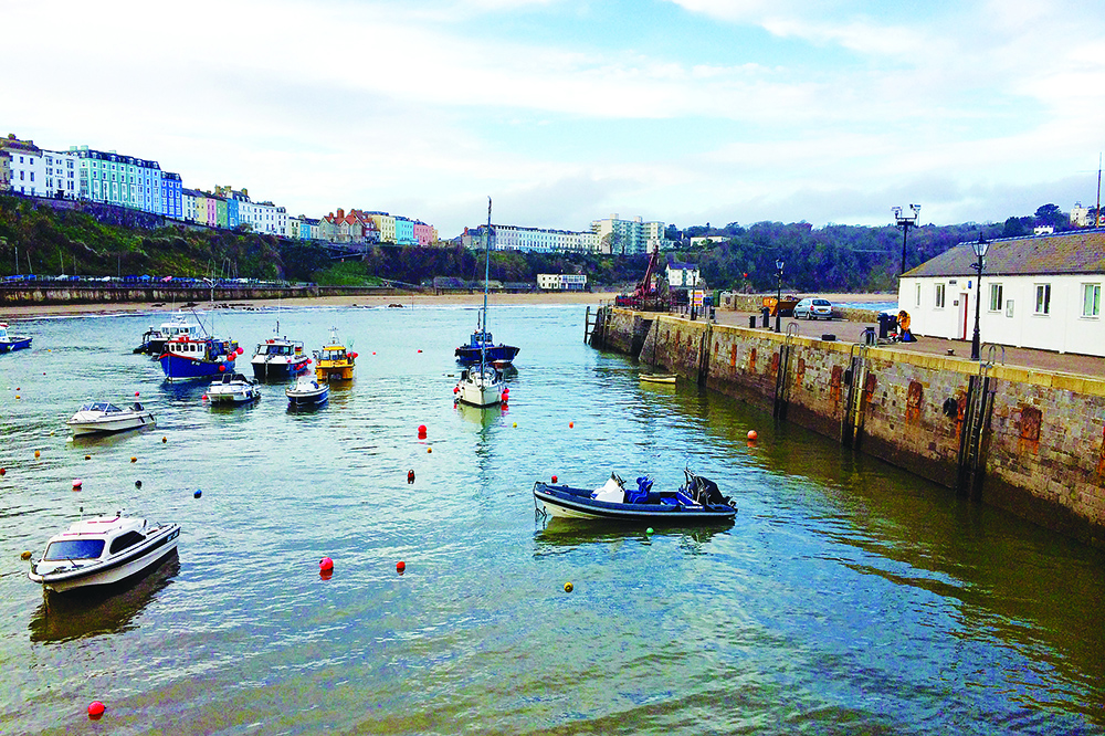 Tenby Harbour at low tide with small boats moored beneath colourful seafront houses.