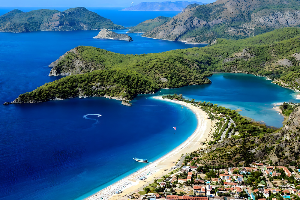 Aerial view of Ölüdeniz Blue Lagoon and Fethiye coastline with turquoise bays, sandy spit and anchored yacht in Turkey’s Aegean.