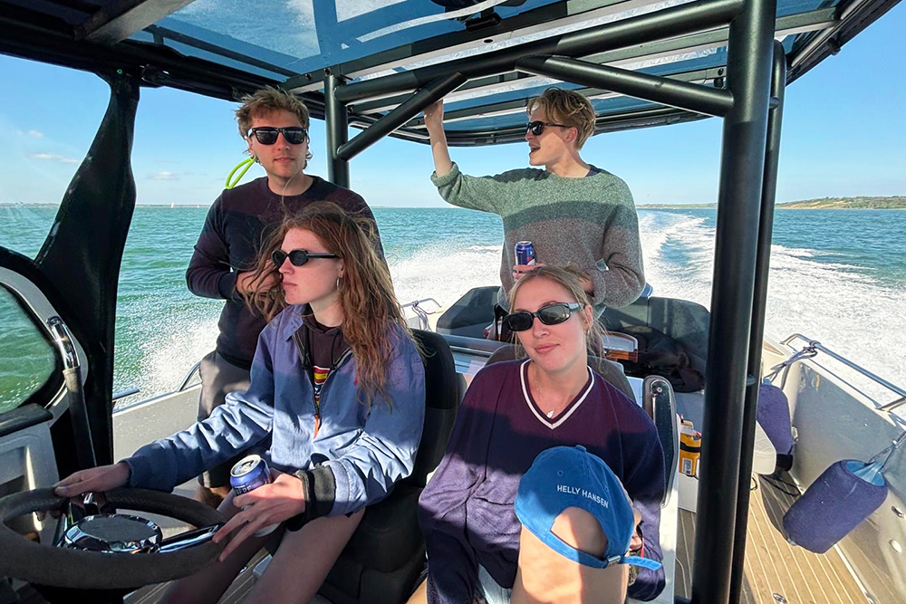 Four young people sat in a T-Top motorbiard facing forwards underway with a wake off the stern