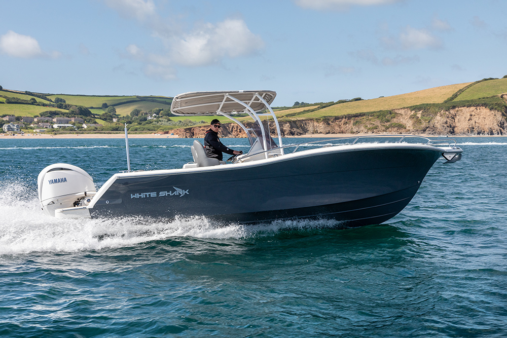 White Shark centre console boat underway with Yamaha outboard, cutting through coastal waters with cliffs in background.