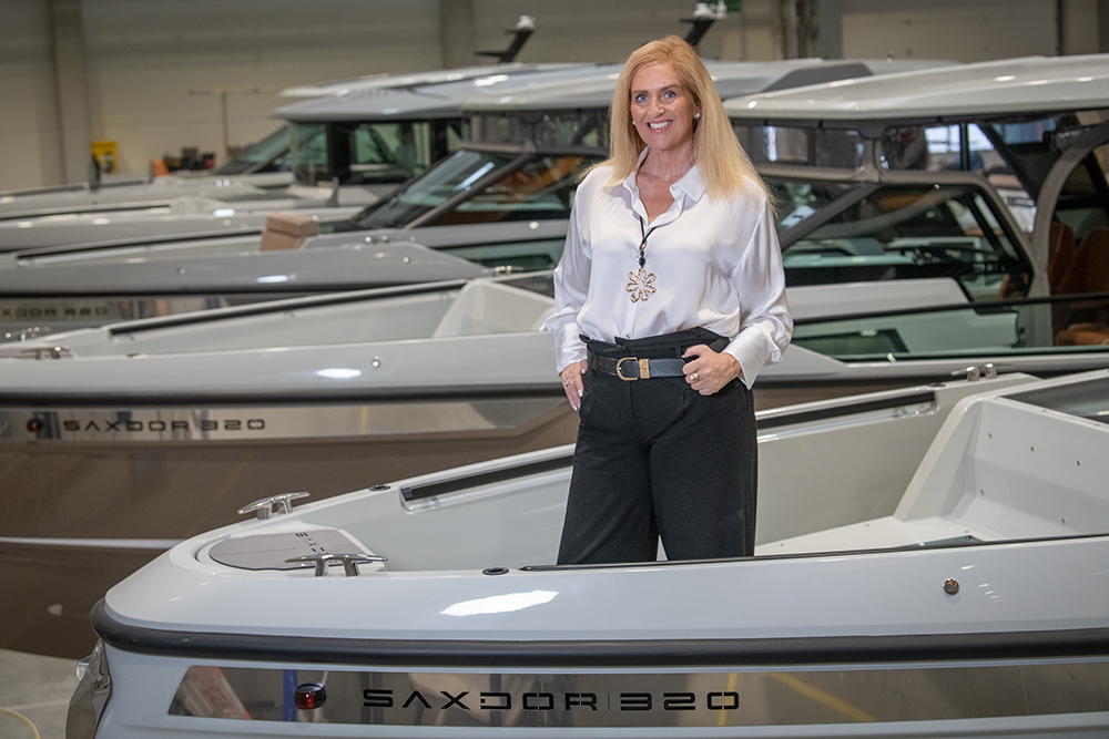 Saxdor executive standing aboard a Saxdor 320 in the production hall, with multiple Saxdor boats lined up behind.