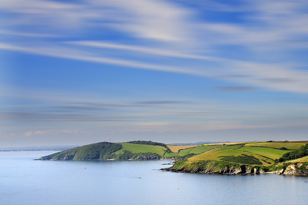 Cornish coastline near Falmouth Harbour with green farmland, cliffs and calm sea.