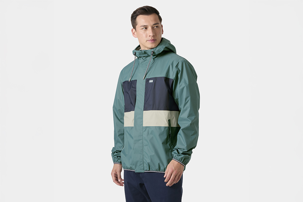 Man wearing Helly Hansen Koster 2.5L waterproof jacket in green and navy, showcasing marine-inspired design and outdoor functionality