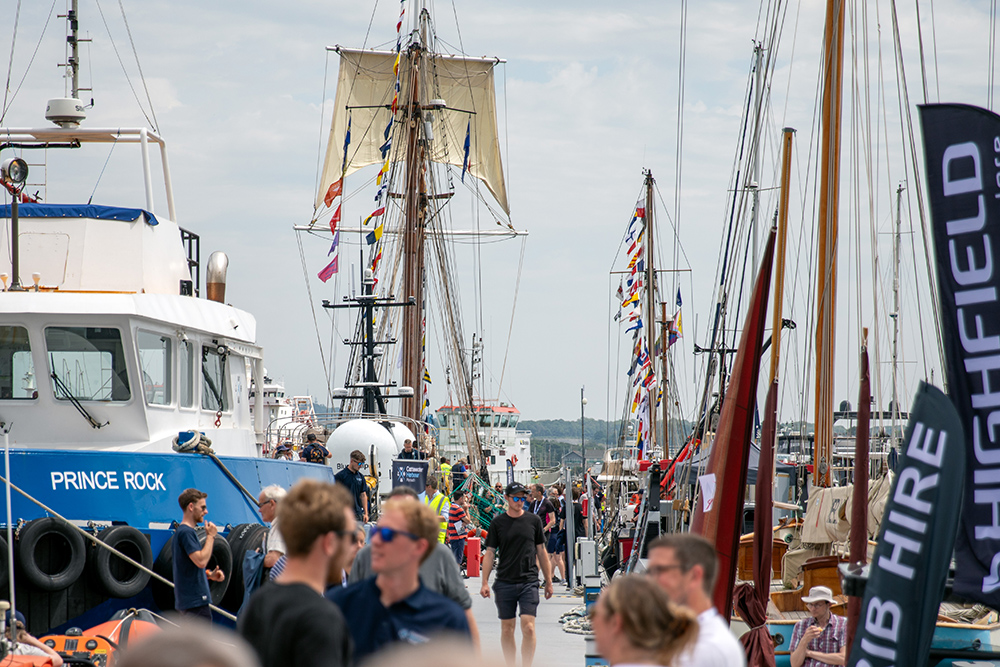 Crowds explore boats and ships along Plymouth marina during Plymouth Boat Fest, with vessels moored and flags flying