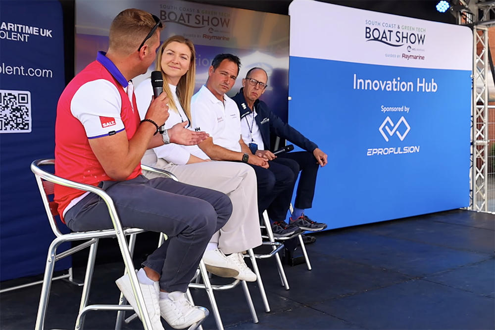 Four people sat on stools on stage with one person talking into a microphone on the Innovation Hub