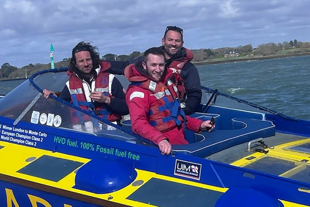 Three crew aboard Apache 555 powerboat during test run, wearing lifejackets, showcasing offshore racing and HVO fuel branding