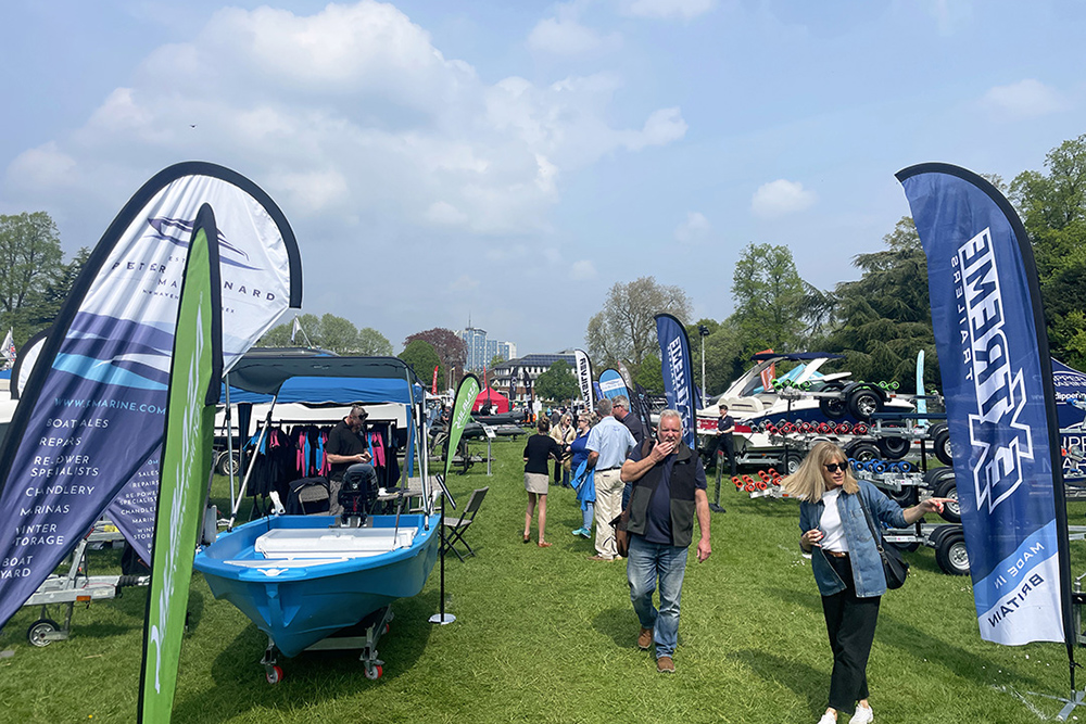 Visitors browsing boats and trailers at outdoor boat show, with exhibitor stands and marine flags on display