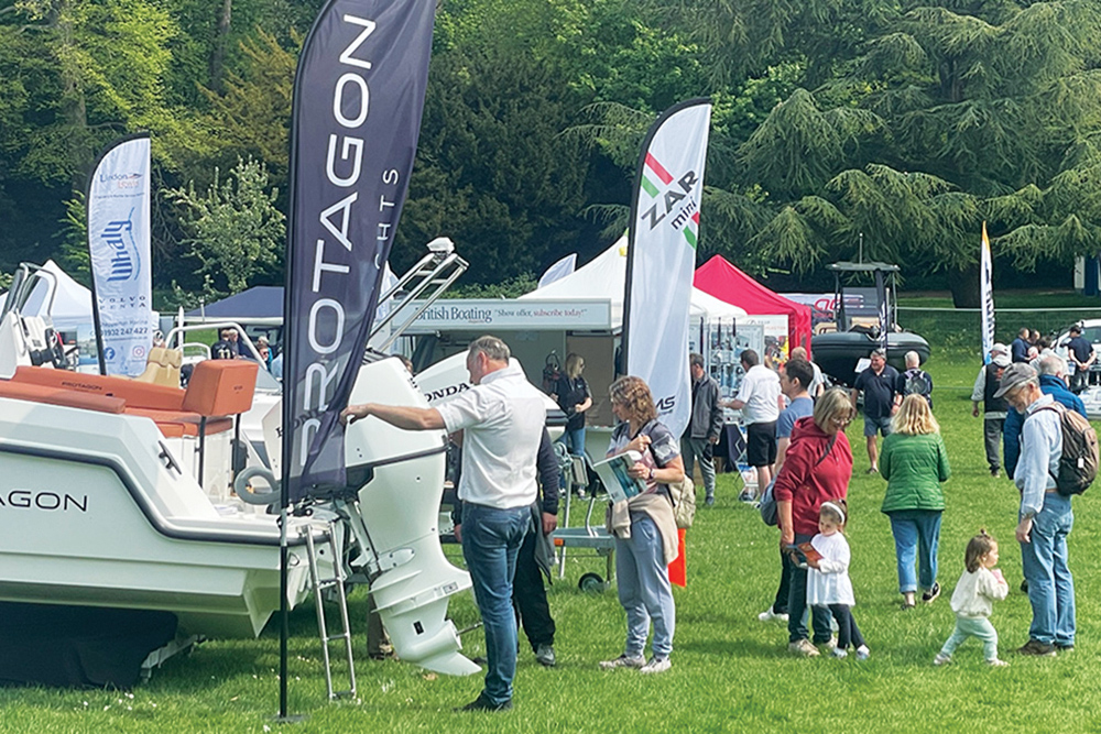 Visitors exploring boats and outboards at outdoor boat show, with families and exhibitor stands on grassy venue