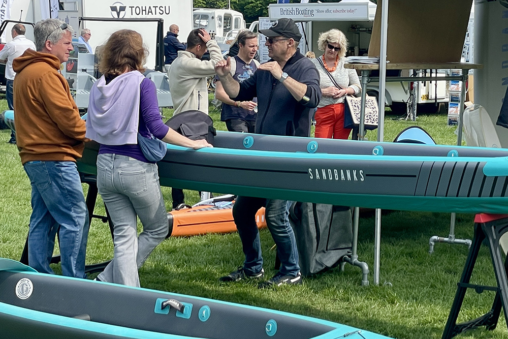 Visitors viewing inflatable paddleboards at boat show stand, discussing features with exhibitors among marine displays