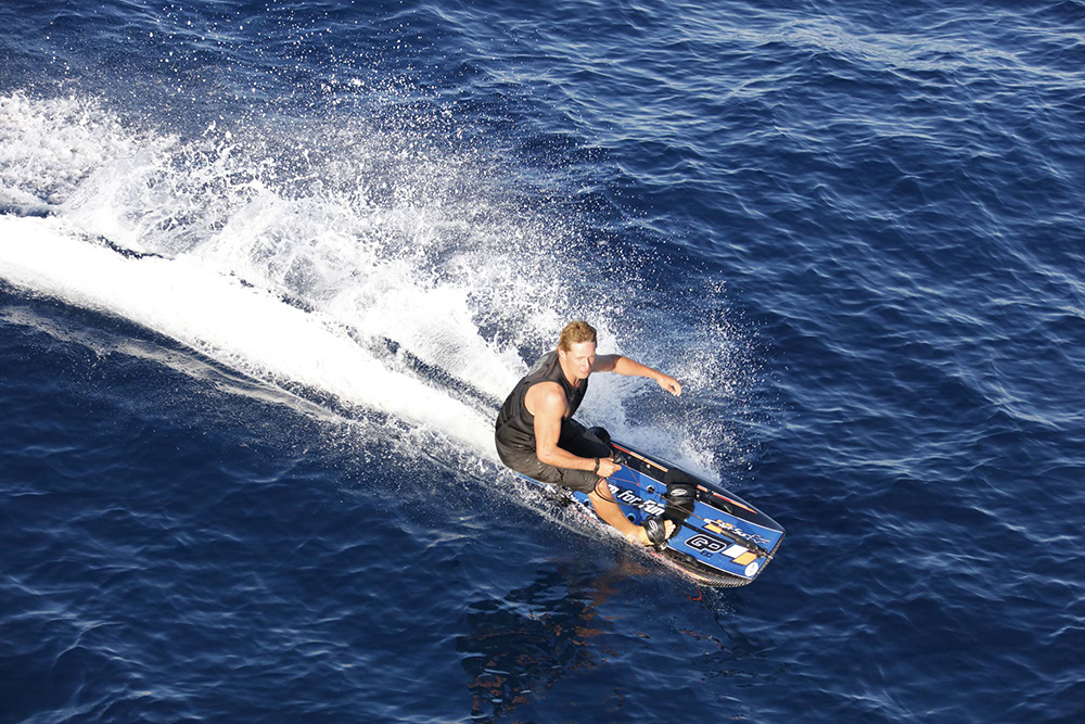 Wakeboarder carving across open water at speed, throwing spray in dynamic watersports action