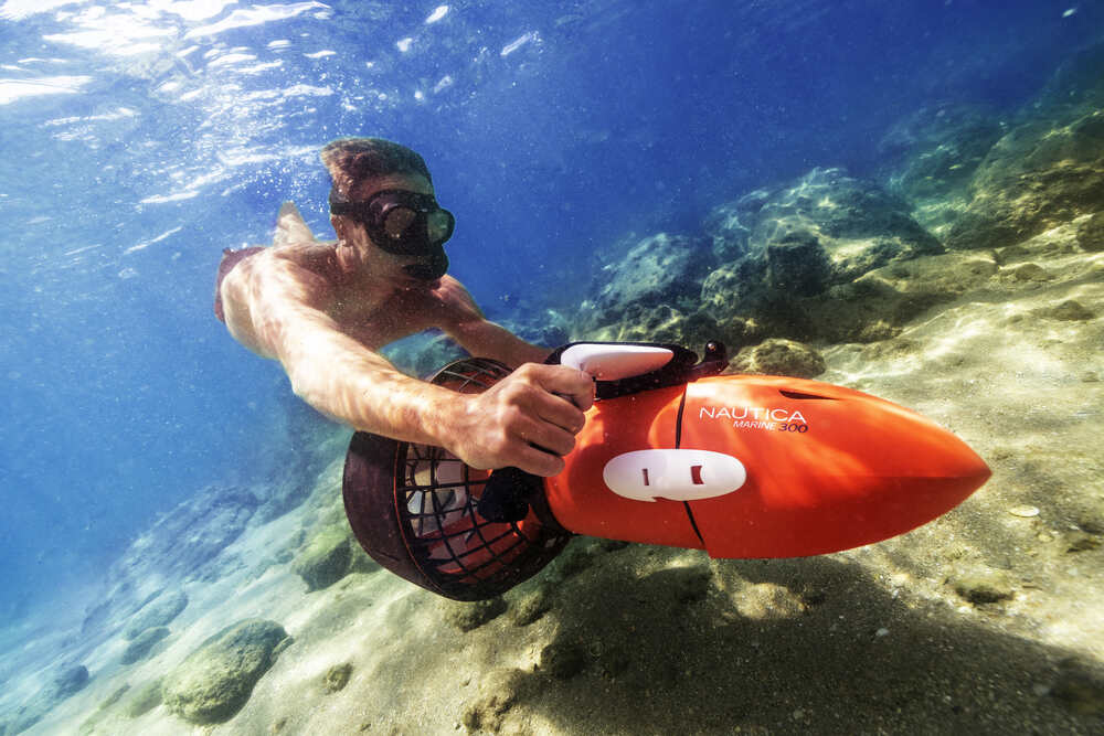 Snorkeller using Nautica Seascooter underwater over rocky seabed in clear coastal water