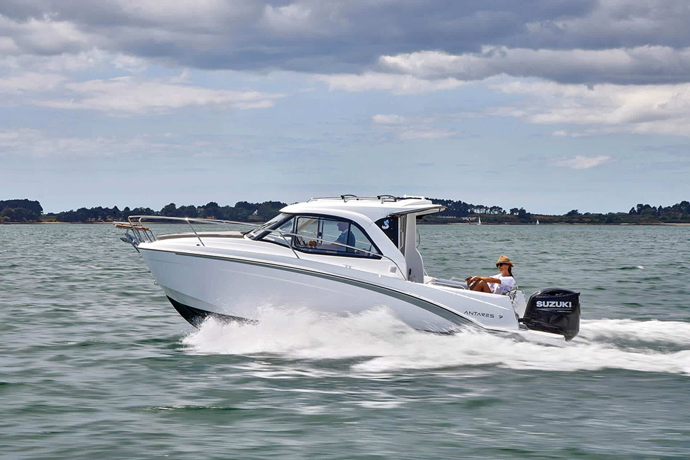 Beneteau Antares 7 cruising at speed with Suzuki outboard, helm enclosed cabin and coastal waters under cloudy skies