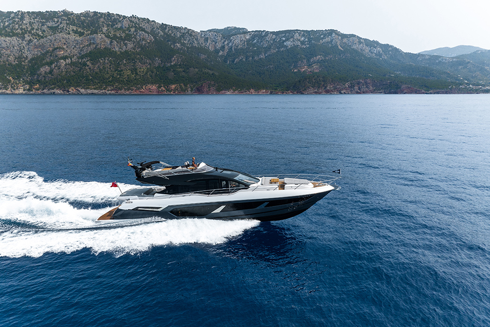 Sunseeker 75 Sport Yacht cruising at speed along a mountainous coastline, showcasing sleek profile and open deck layout.