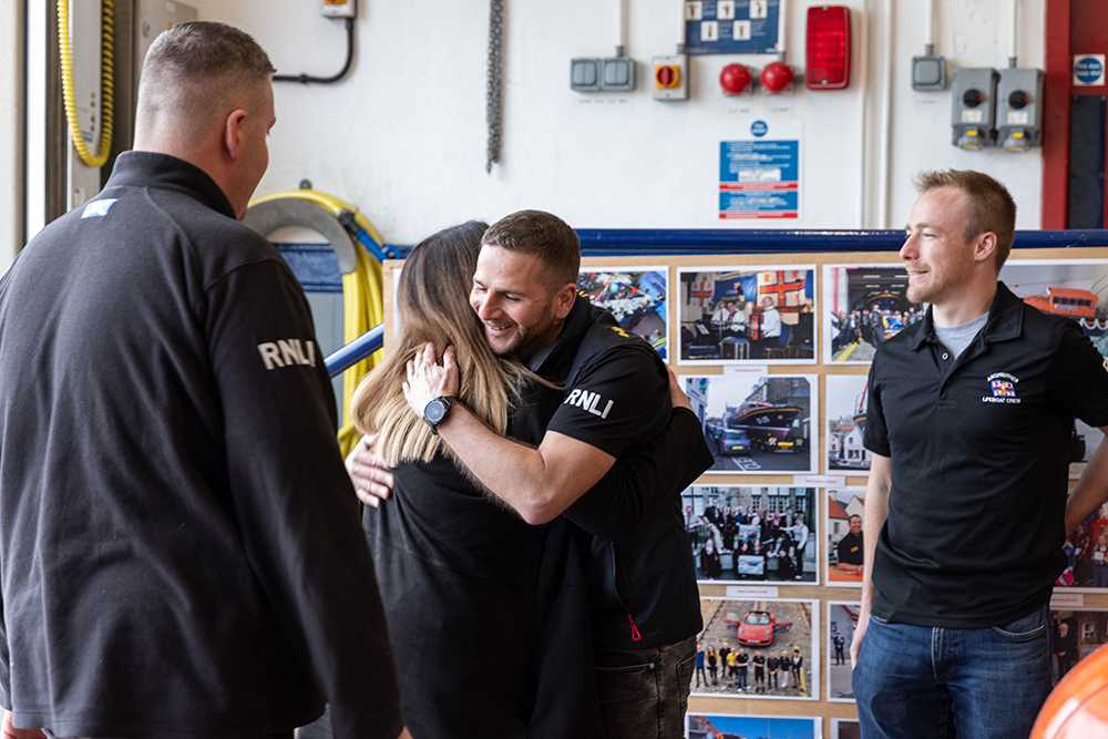 RNLI crew member embraces rescued woman inside lifeboat station, highlighting rescue reunion and volunteer lifesaving efforts.