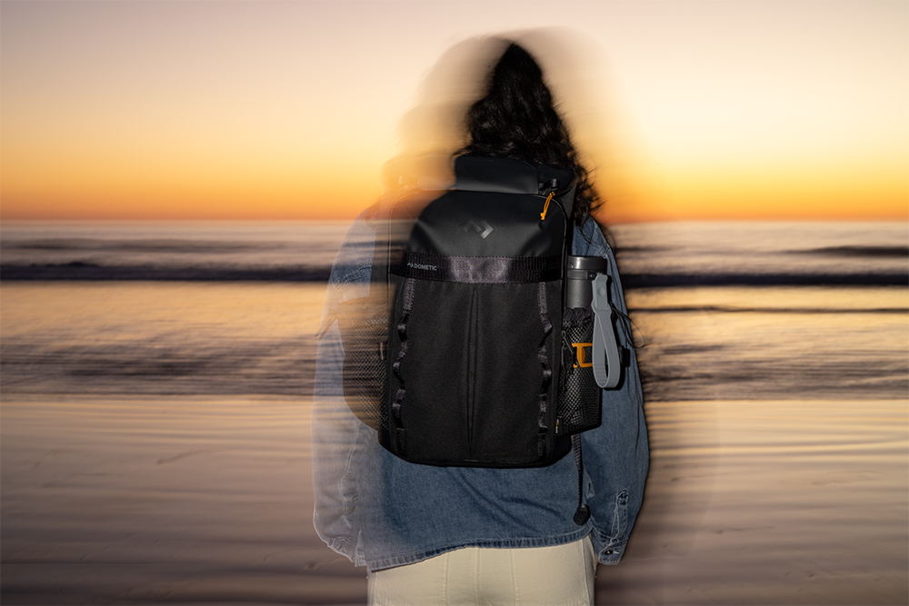 Person wearing Dometic cooler backpack on beach at sunset, highlighting compact design and everyday carry use