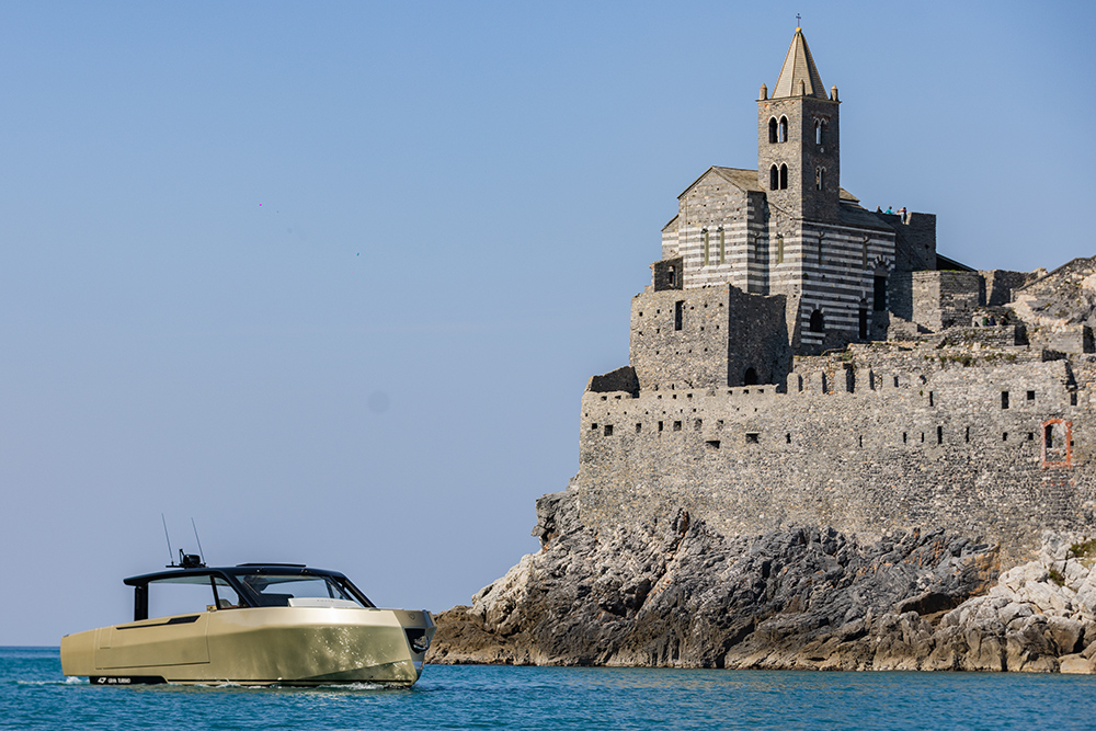 Forte 47 Gran Turismo cruising past coastal stone church on rocky shoreline, highlighting sleek design.