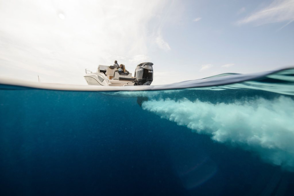 Split-level view of a motorboat with Suzuki outboard, showing underwater prop wash and surface cruising above.
