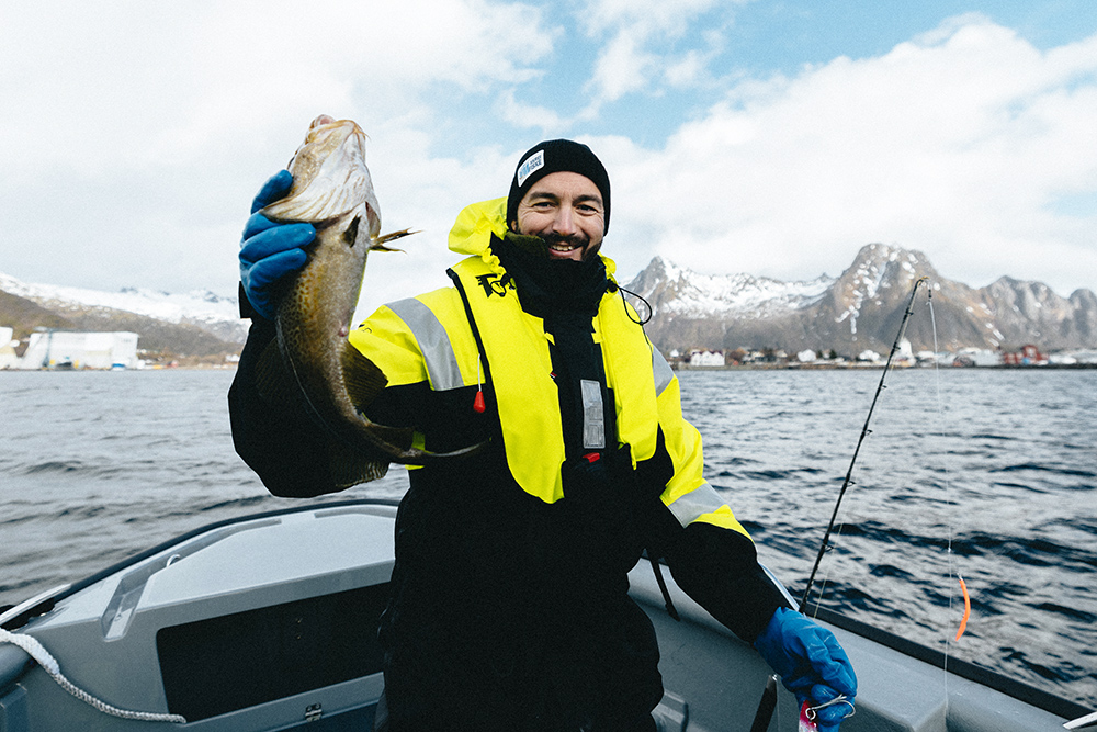 Fisherman holding up cod in the bow of a boat