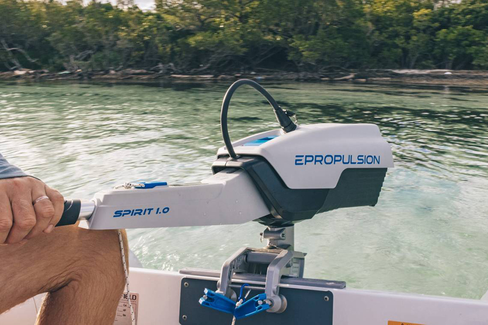 ePropulsion Spirit 1.0 electric outboard on small boat, showing tiller control and removable battery on calm water.