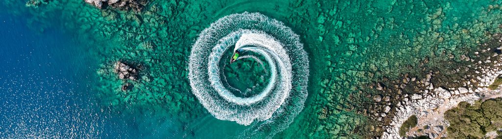 Motorboat circling round and round creating a white wash within rocky outcrops on mediterranean sea