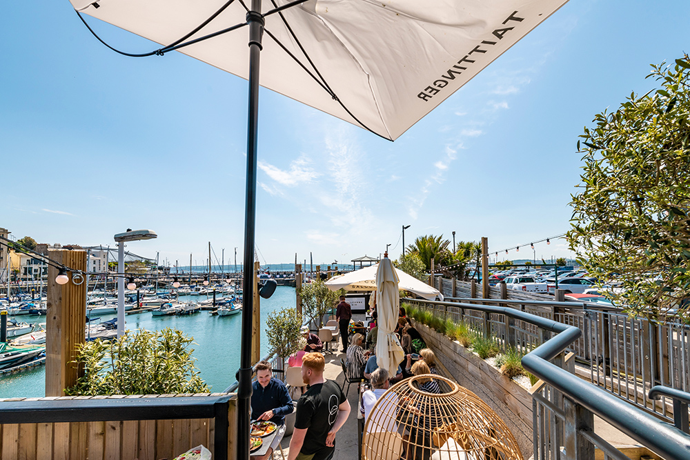 People eating out in a waterside cafe with marina boats in the background
