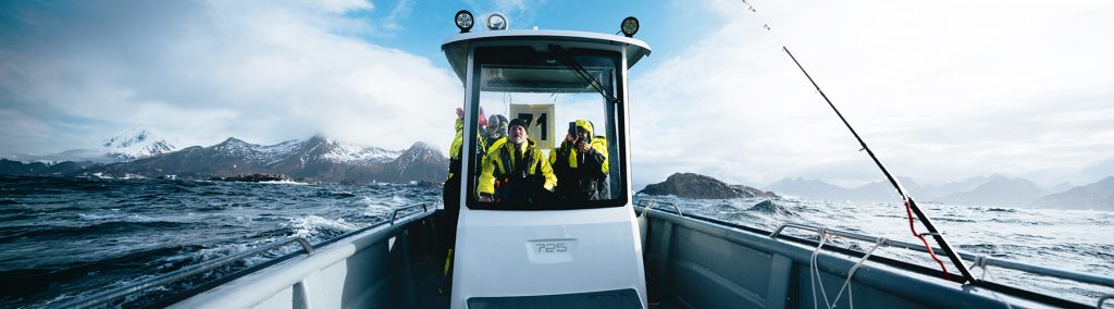 Several boaters in heavy weather clothing behind a T-top of a open Sting 725 facing forwards with mountains in the background