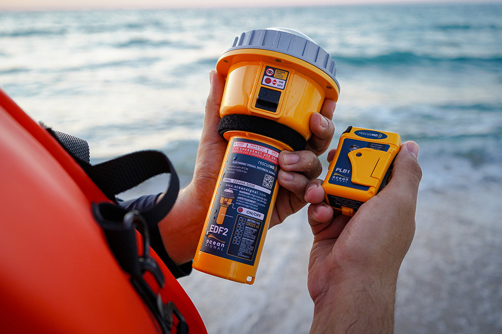 Man holding a Ocean Signmal electronic flare and personal locator beacon device in his hands with a sea background whilst wearing a lifejacket