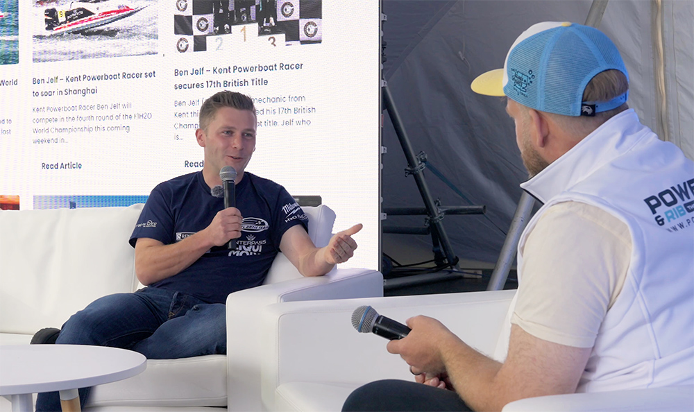 Monty interviewing Ben Jelf on white sofas holding microphones with a PBR backdrop