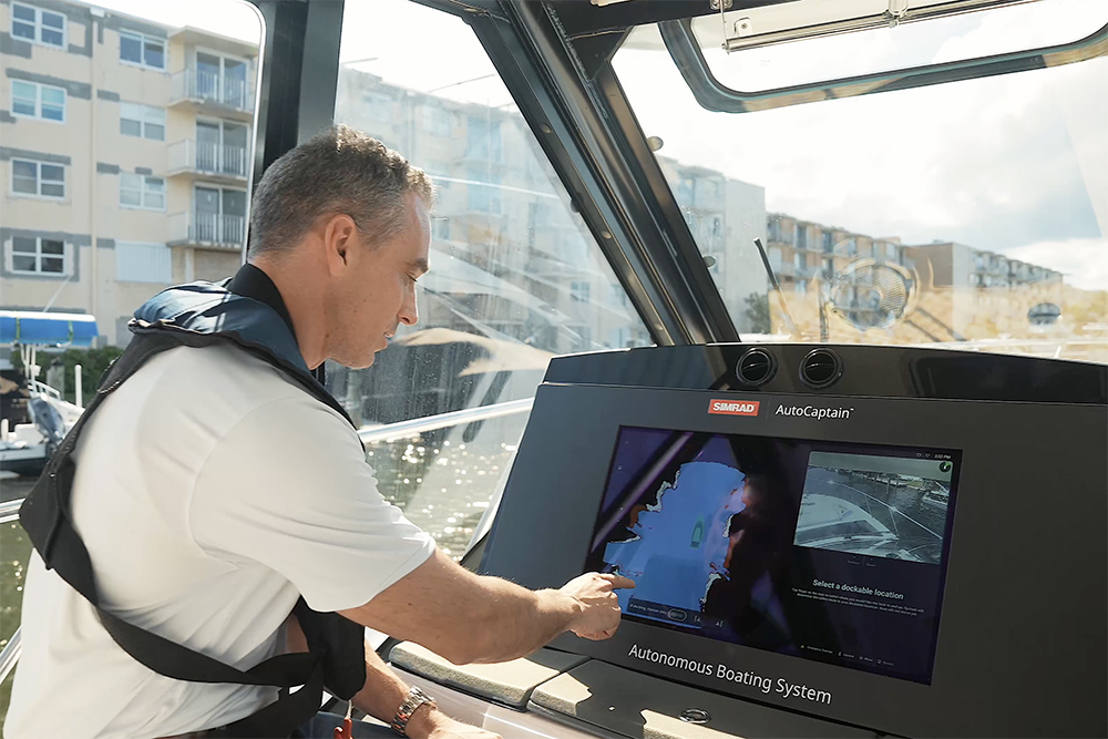 Man at helm using the touch screen of a Simrad multi function screen to operate autonomous docking system