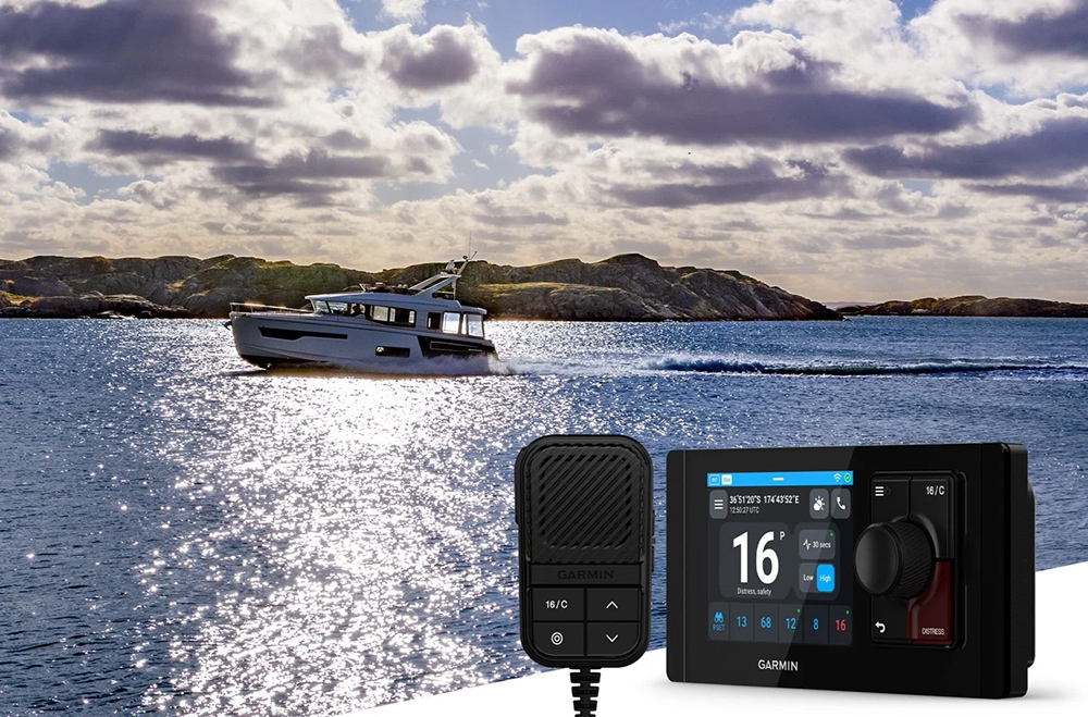 Garmin Signal VHF radio and handset shown over a coastal motorboat scene with rocky shoreline and bright sea reflections.