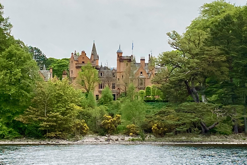 Aldourie Castle seen from Loch Ness, framed by woodland on the Highland shoreline