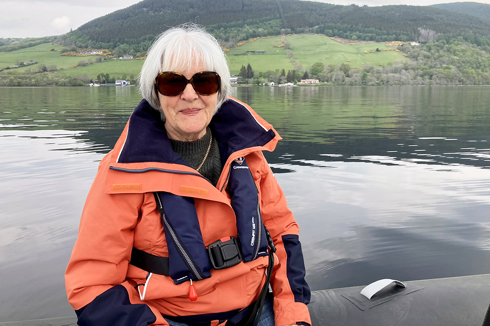Crew member aboard a RIB on calm Loch Ness, wearing lifejacket with Highland shoreline behind