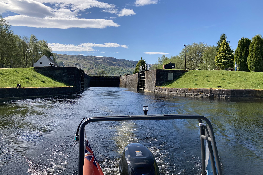 RIB leaving a Caledonian Canal lock beside an old keeper’s cottage under clear Highland skies