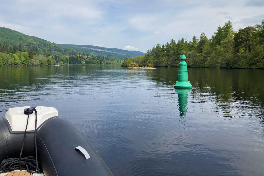 RIB entering Loch Dochfour from Loch Ness, passing a green channel marker amid Highland woodland