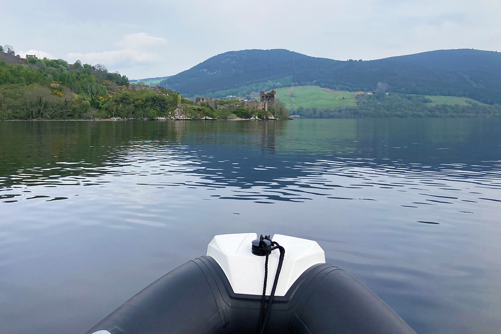 RIB approaching Urquhart Castle on calm Loch Ness, with Highland hills beyond