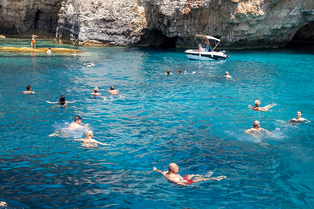 A coastal bay with swimmers of all ages in the sea and a boat at anchor