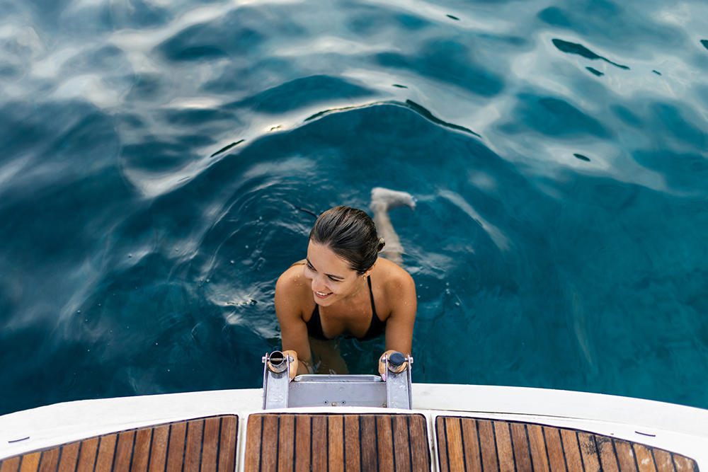 Beautiful woman is climbing ladders on a sailboat, getting out of the sea. The sea is beautiful turquoise color.