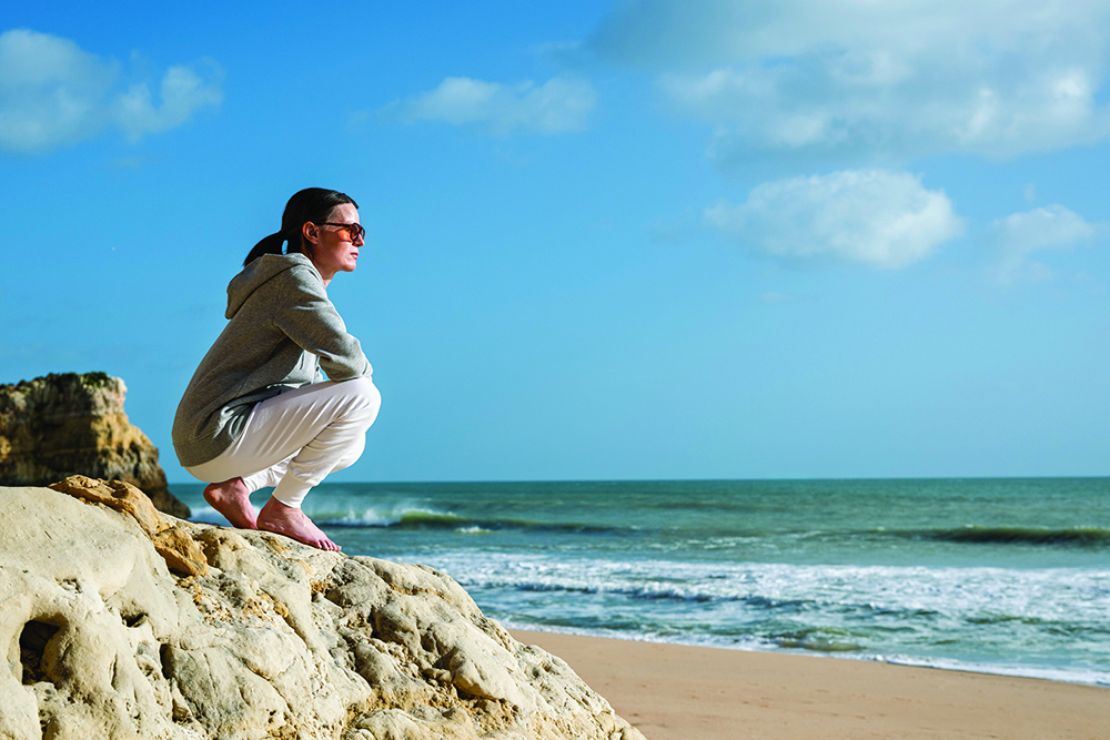 sporty woman sitting on rocks by the sea looking at the view