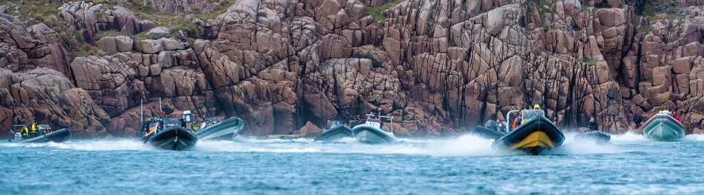 Multiple rigid inflatable boats underway underneath a cliff face