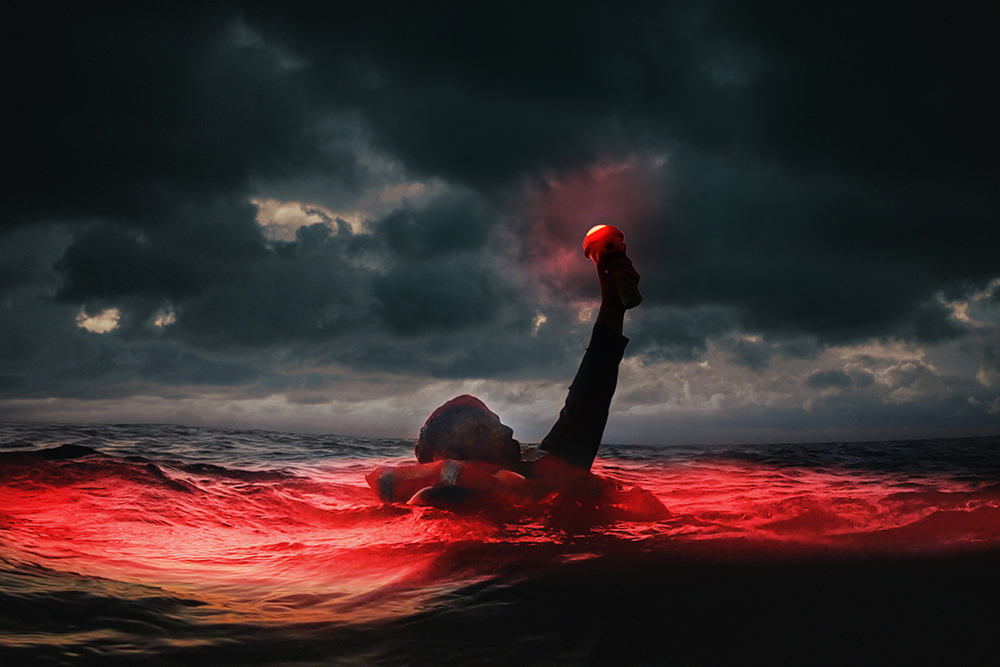 Person in rough seas raises red distress flare under storm clouds during marine emergency