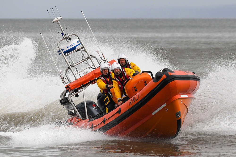 RNLI lifeboat crew powering an orange inshore rescue boat through rough seas.