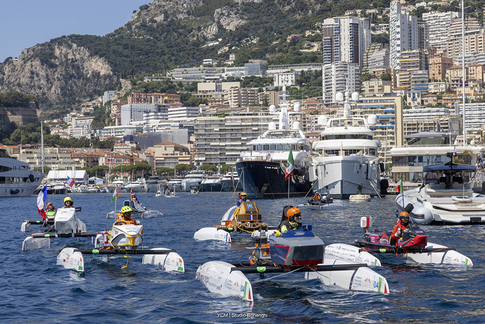 Monaco Energy Boat Challenge teams race prototype boats past superyachts in Monaco harbour.