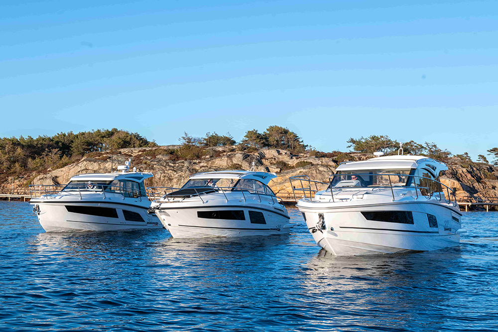 Three Finnmaster motorboats cruising beside a rocky Nordic shoreline.