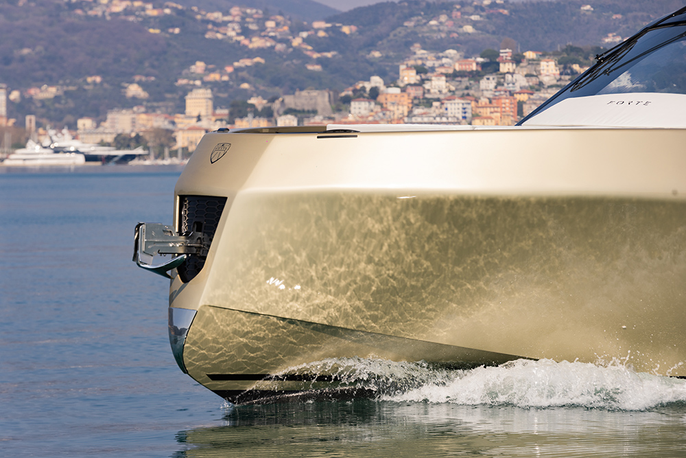 Forte 47 Gran Turismo bow cutting through calm water with coastal town backdrop