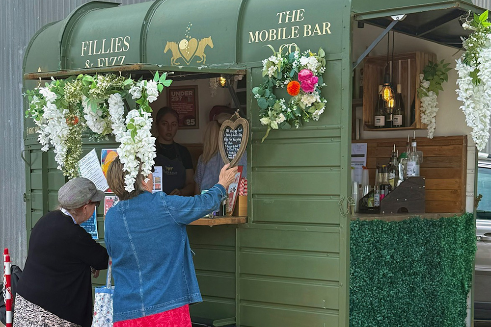 Mobile bar serving visitors at Plymouth Boat Fest with floral decoration and event stalls nearby.