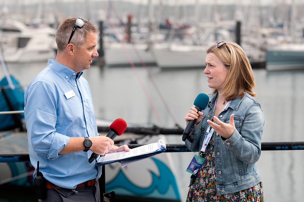 Interview at Plymouth Boat Fest with two presenters holding microphones beside the marina.