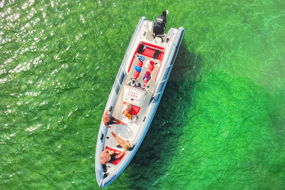 Aerial view of the Peaky Blinder RIB with people aboard in clear green water.