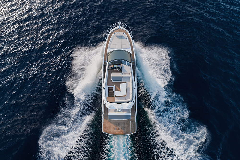 Overhead view of a flybridge motor yacht cruising at speed, open flybridge deck and helm visible, wake fanning out behind.